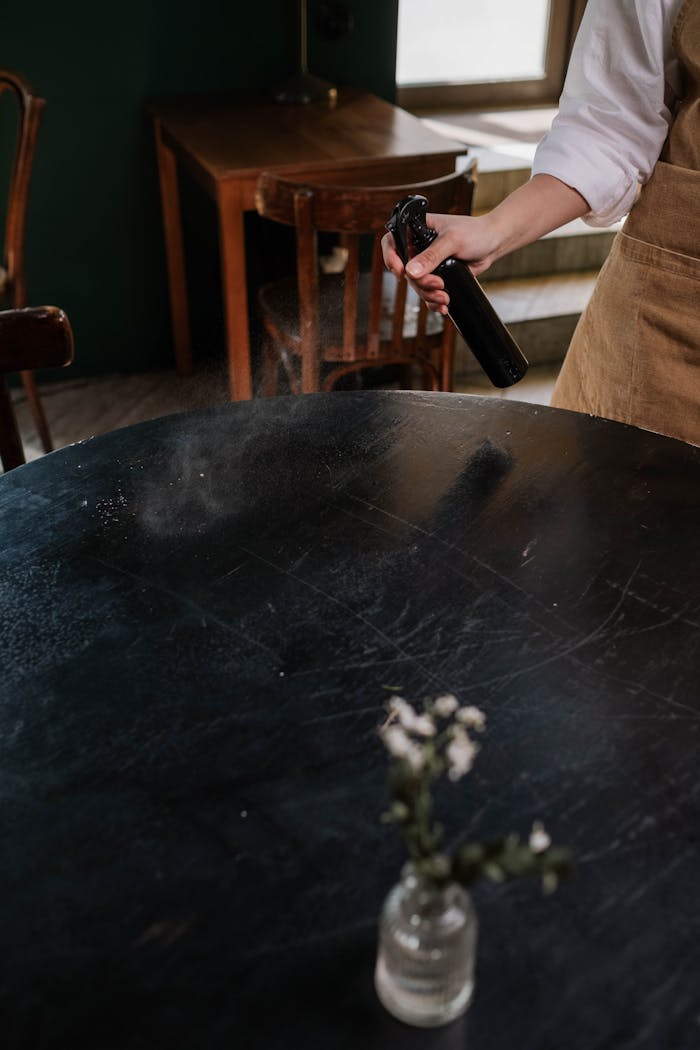 A waitress cleans a table with a spray bottle in a cozy café setting.